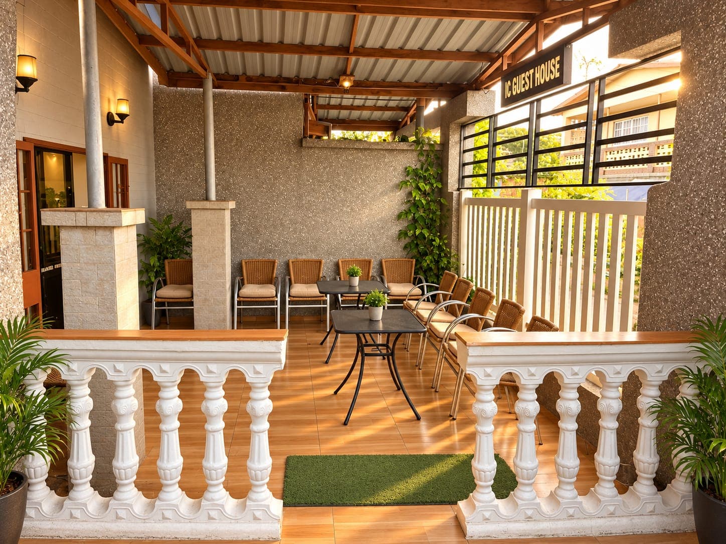 The covered front terrace at JC Guest House at sunset, with wicker chairs and the guest house sign